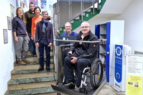 Behindertenbeauftragter Rudi Bamberger und Bürgermeister Dr. Ralf Göck (v.l.n.r.) weihten den Treppenlifter mit der Büchereibelegschaft um Büchereichef Christian Sauer (Mitte) und seine Mitarbeiterinnen Luisa Uhrig (l.) und Ute Roes sowie Kai Rill ein